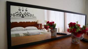 Een hotelkamer met een bed, nachtkastje, lamp en een spiegel die de kamer weerkaatst.
