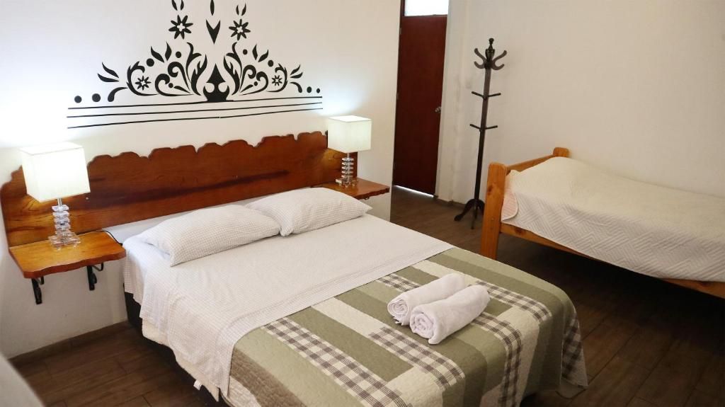 A hotel room with a bed, a bedside table with a lamp, a coat rack, and a bench.