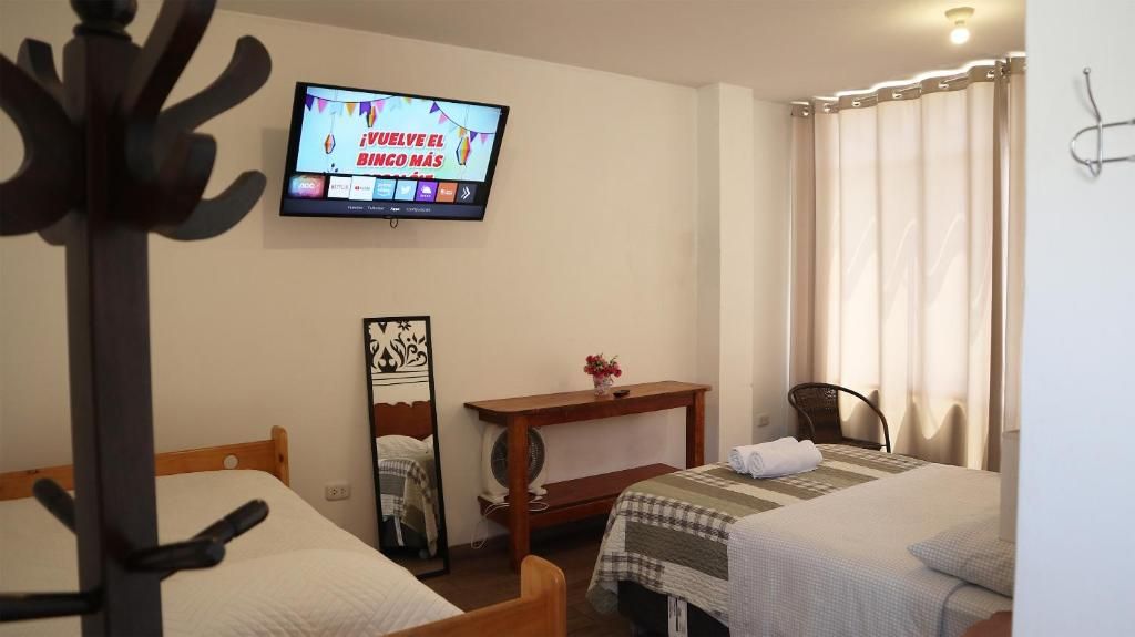 A hotel room with two beds, a TV mounted on the wall, a wooden nightstand, and a window with curtains.