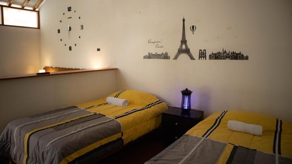 A hotel room with two beds, a wall clock, and a decorative wall with Paris landmarks.