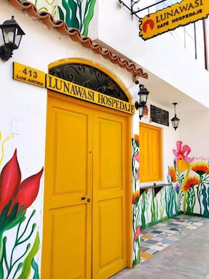 Un edifici amb una porta groga amb la inscripció 'LUNAWASI HOSPEDAJE' i un senyal que indica l'adreça '413 LOS ANDES'.