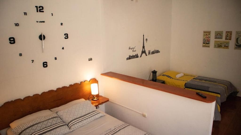 A hotel room with a bed, a nightstand with a lamp, a wall clock, and a bed with a yellow blanket.