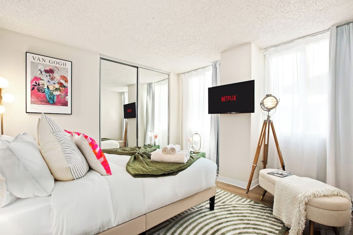 Une chambre d’hôtel avec un lit, une télévision, un trépied et une œuvre d’art encadrée accrochée au mur.