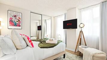 Une chambre d’hôtel avec un lit, une télévision, un trépied et une œuvre d’art encadrée accrochée au mur.