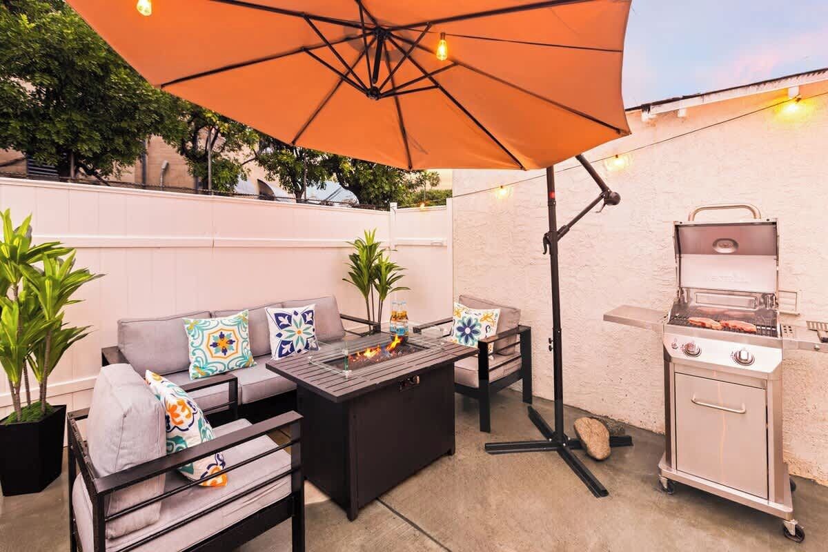 An outdoor patio with a barbecue grill, a sofa set, and a large umbrella providing shade.