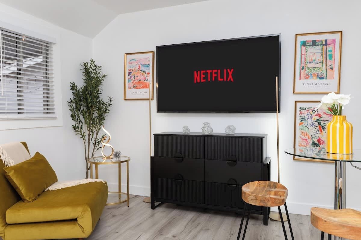 Ein Wohnzimmer mit einer Couch, einem an der Wand befestigten Fernseher, einem kleinen Beistelltisch und einem Schrank.