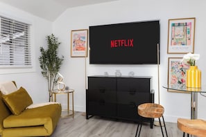Een woonkamer met een bank, een aan de muur bevestigde televisie, een klein bijzettafeltje en een kast.