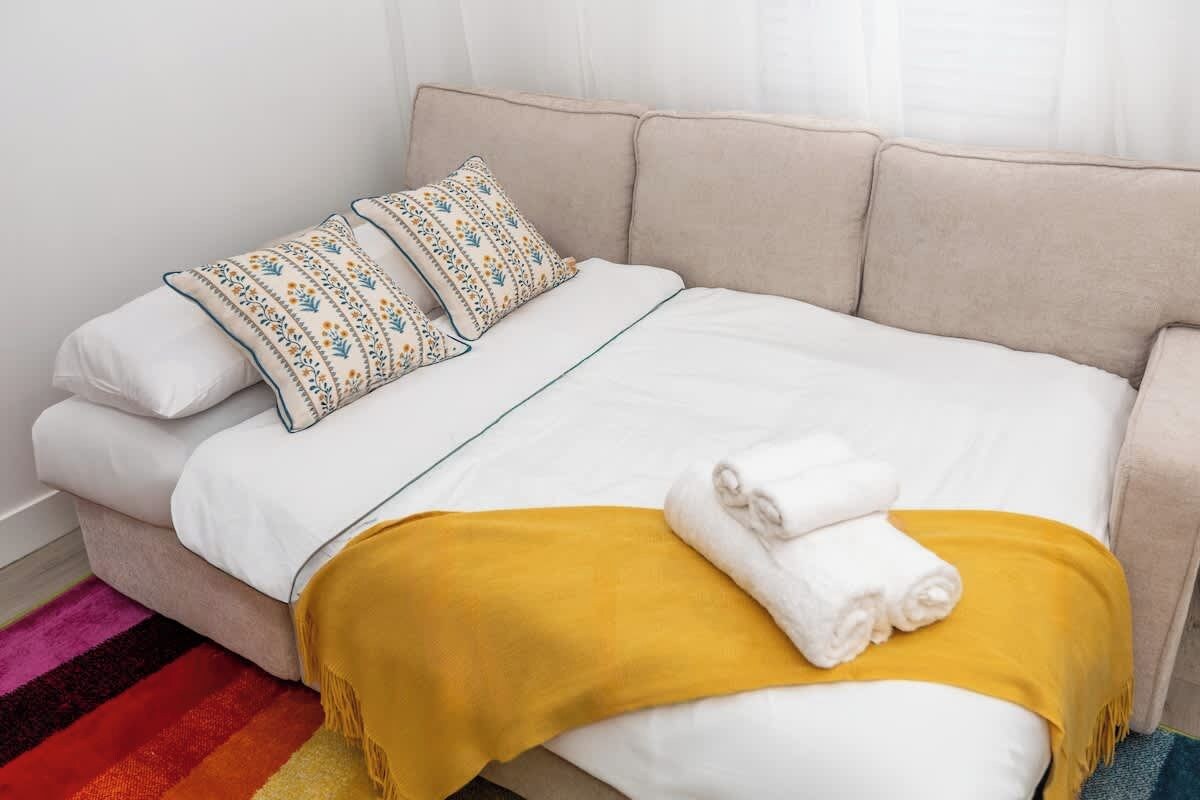 Een bed met wit beddengoed, twee gestreepte kussens, een gele deken en twee opgevouwen handdoeken.