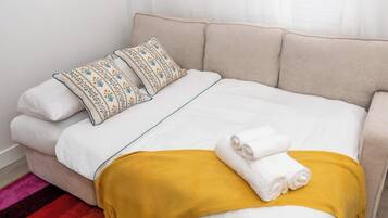 Een bed met wit beddengoed, twee gestreepte kussens, een gele deken en twee opgevouwen handdoeken.