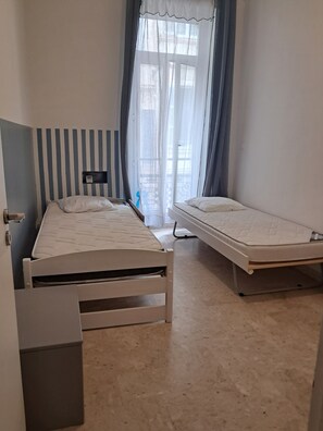Quarto com cama, uma mesinha e janela com cortinas.