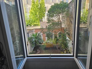 A view from a window with a balcony, overlooking a courtyard with trees and a building with a tiled roof. - Marseille, 5th arrondissement: 140 m² duplex + garden + air conditioning (Marseille)