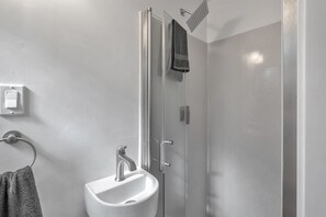 Een badkamer met een douche met glazen wanden, een wit wastafeltje en een handdoek aan een rek.