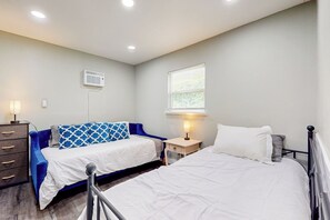 A bedroom with two beds, a dresser, a bedside table with a lamp, a window with blinds, and an air conditioning unit on the wall. - Peace at the River -Private Dock, Games, & FirePit (Bethel Island)
