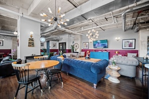 A modern interior with a blue sofa, wooden dining table, and chairs, a TV, and exposed ductwork. - The Bentley Collection - The Landmark Loft (Dallas)