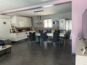 Eine moderne Küche mit weißen Schränken, einer Essecke mit schwarzen Stühlen und einem großen Kühlschrank.