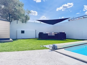 Ein Garten mit Pool, Sitzgelegenheit mit Tisch und Stühlen und einem Rasen.