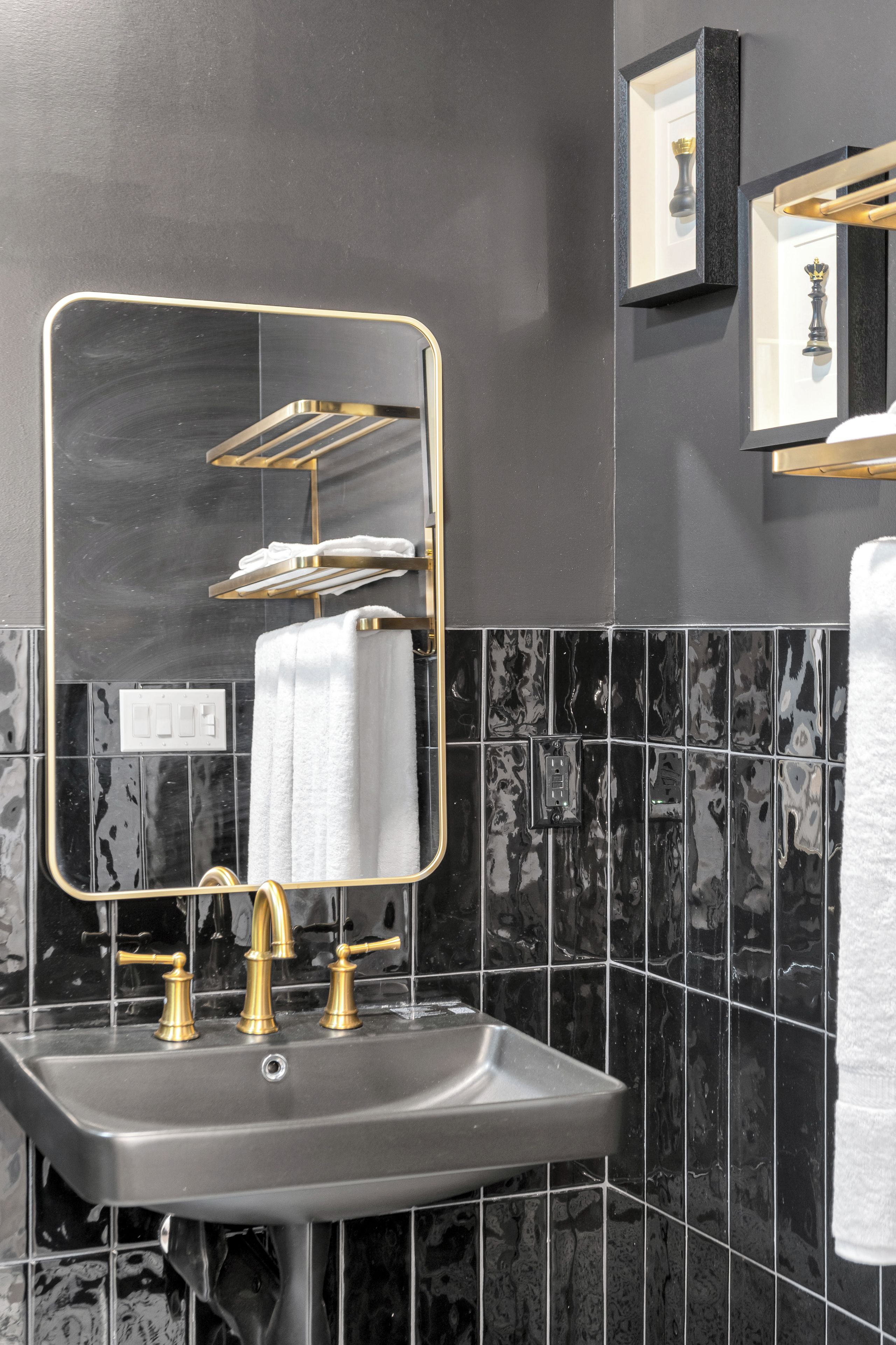 A bathroom with a gold-framed mirror, a sink with gold faucets, and black marble tiles.