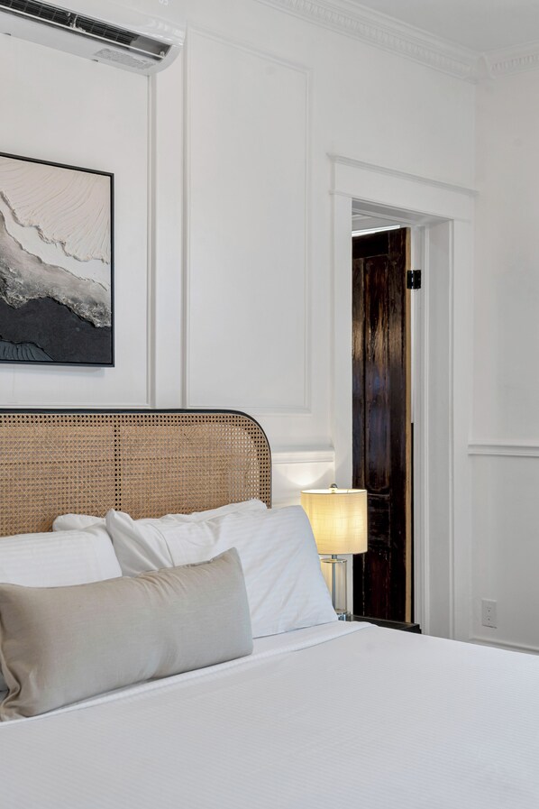 A hotel room with a bed, a headboard, a lamp, and a door.