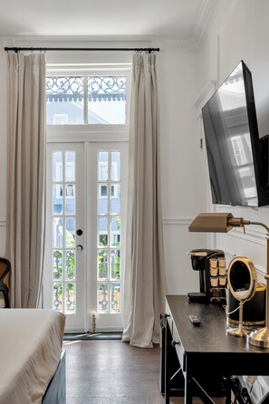 A hotel room with a bed, a desk with a coffee machine, a TV, and a large window with curtains.