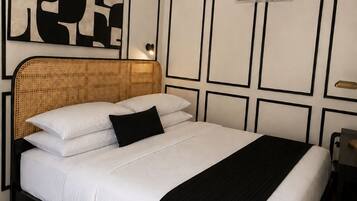 Un lit bien fait, avec une tête de lit noire, une literie blanche et un plaid noir.