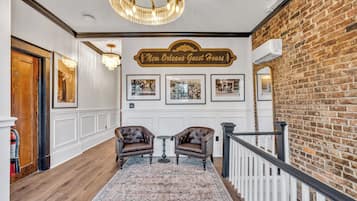 A hallway with a chandelier, two armchairs, a rug, and a sign reading 'New Orleans Guest House'.