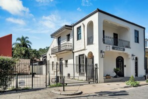 A two-story hotel with a white facade, balconies, and a gated entrance.