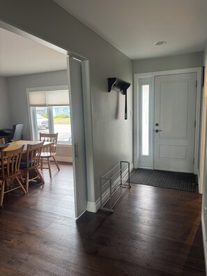 Una habitación con una mesa de comedor y sillas, una puerta con felpudo y una ventana con persianas.