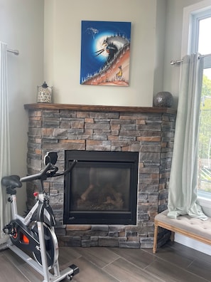 A room with a stone fireplace, a mounted exercise bike, and a painting on the wall. - Spacious 4-bedroom house in beautiful Elliot Lake. Close to all trails and town. (Elliot Lake)