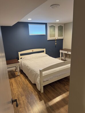Un dormitorio con cama, mesita de noche, cómoda, ventana con persianas e iluminación en el techo.