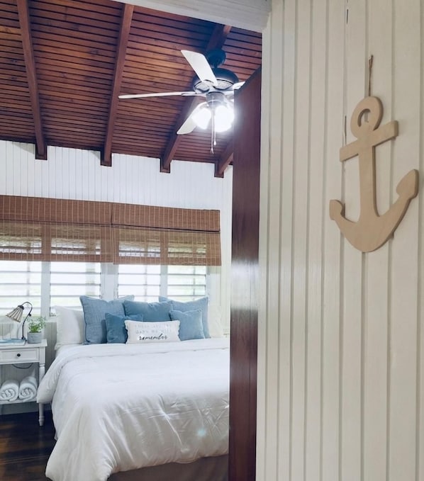 Een slaapkamer met een bed, een plafondventilator, een aan de muur bevestigde decoratie en een raam met zonwering.