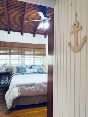 A bedroom with a bed, a ceiling fan, a large anchor decoration, and a window with blinds.
