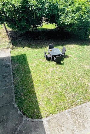 Un área exterior con césped, una mesa y sillas, rodeada de abundante follaje.