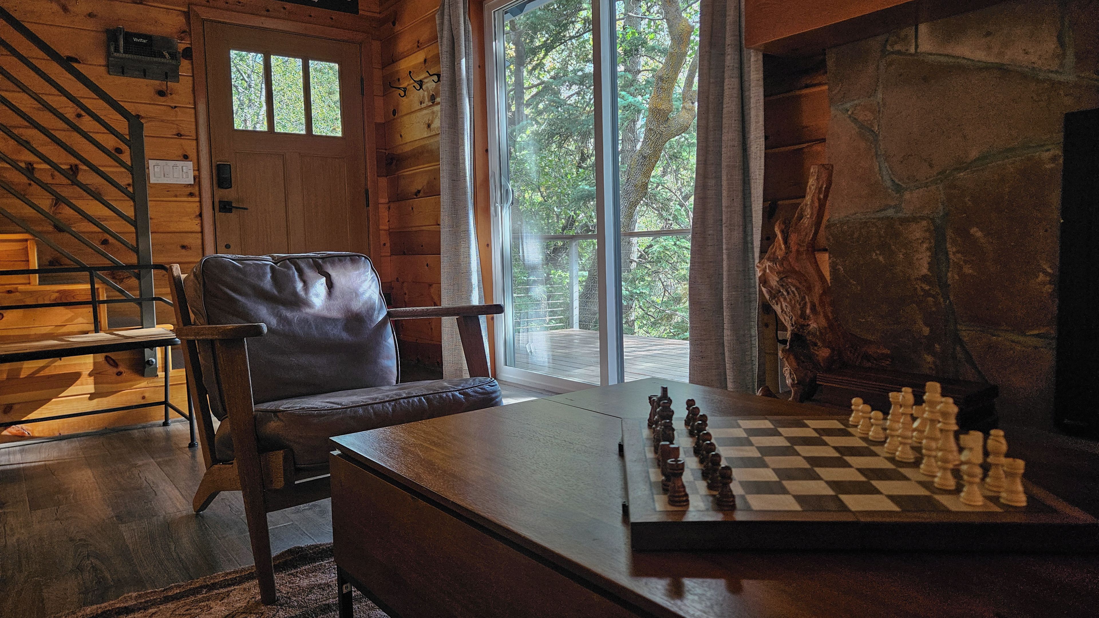A wooden interior with a chessboard, a leather chair, and a staircase.