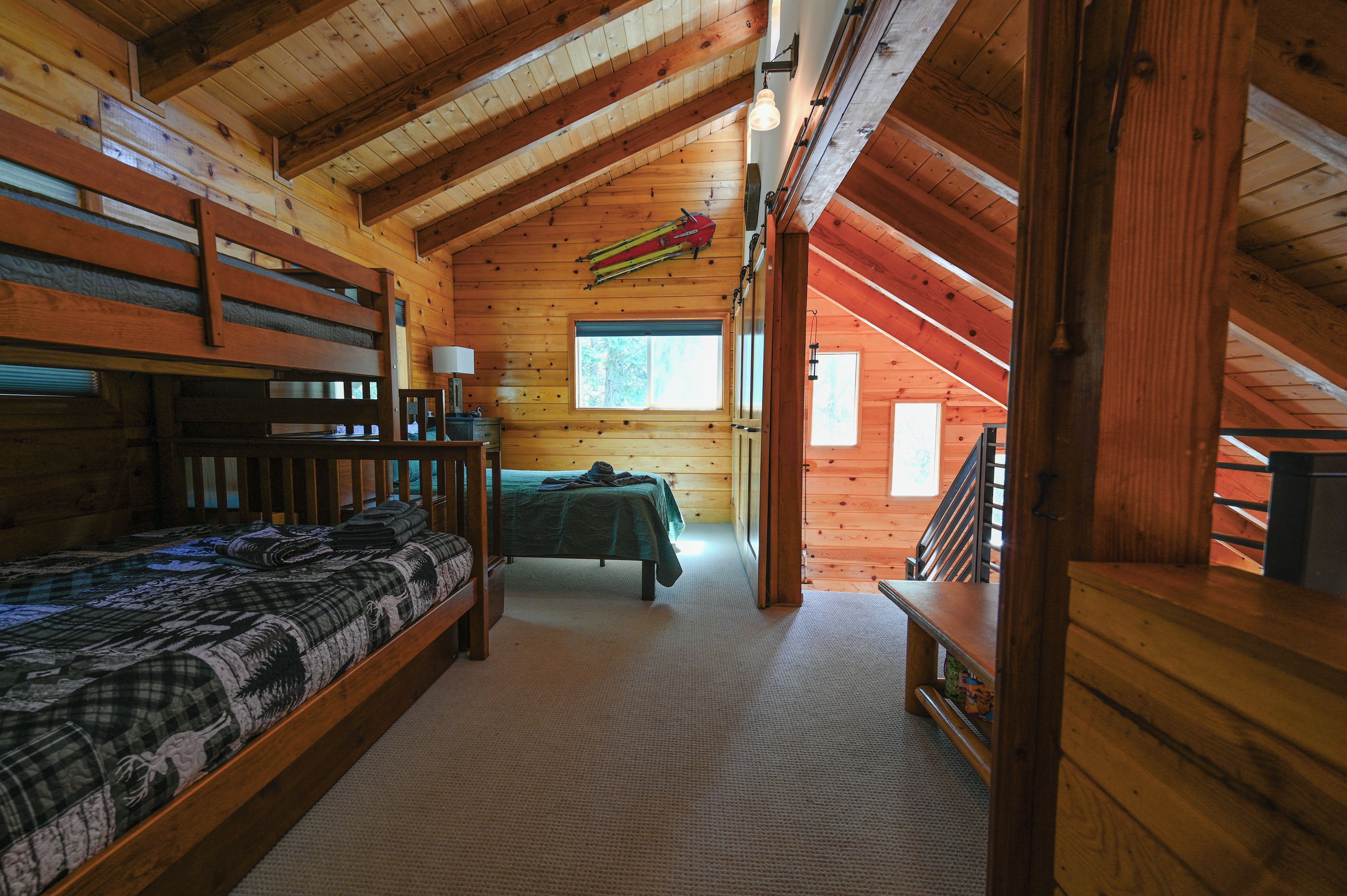 A cabin interior with a loft bedroom, a bunk bed, and a view of the outdoors.