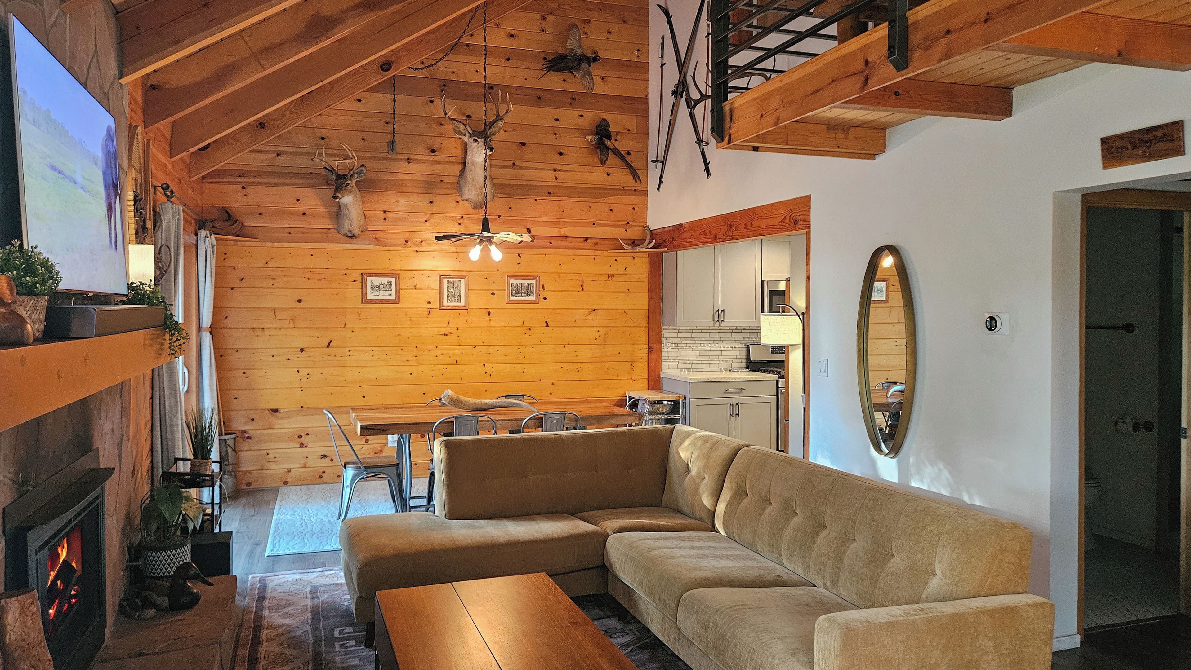 A cozy interior with a wooden ceiling, a fireplace, a sofa, a dining area, and a kitchen.