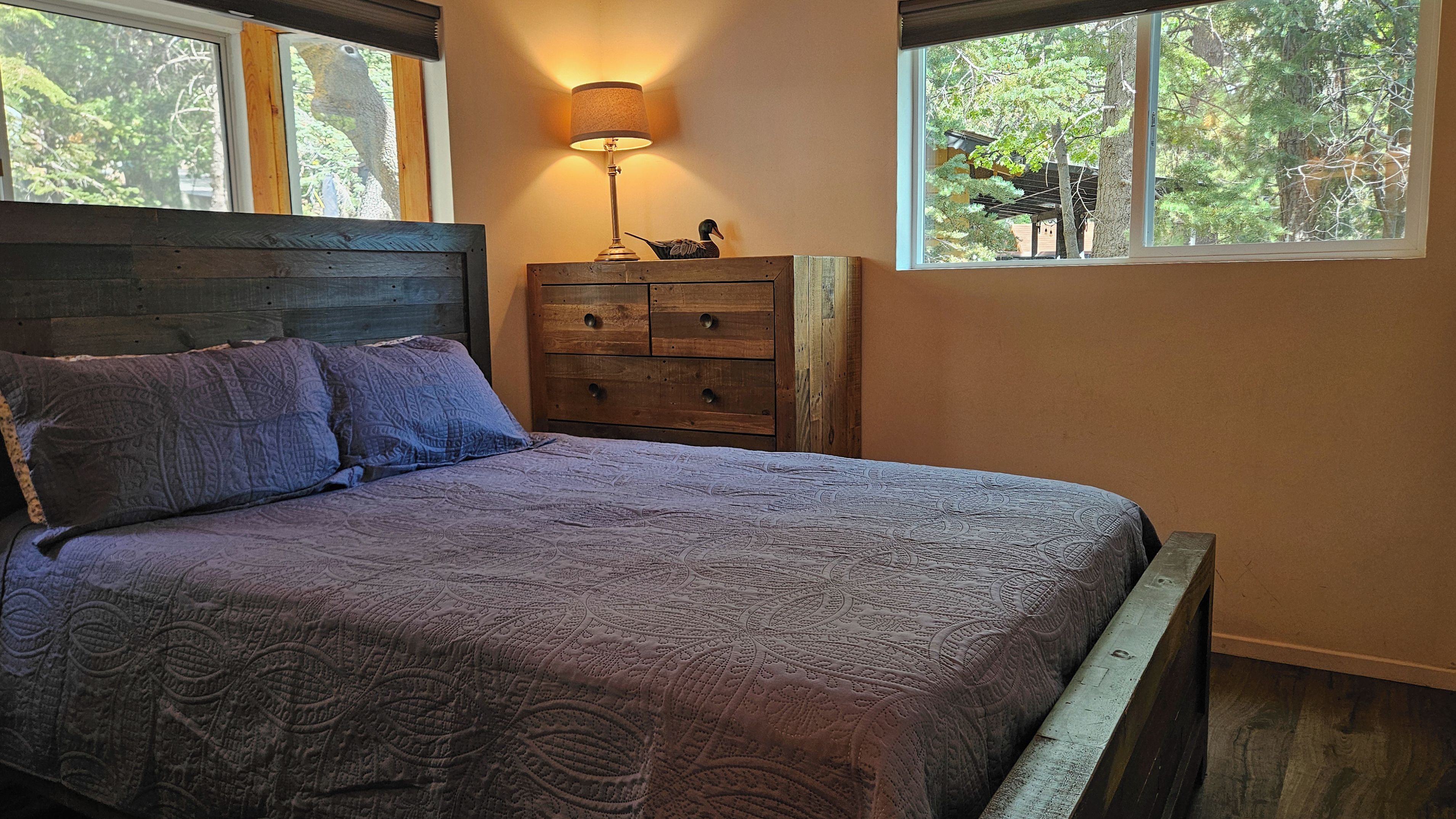 A bedroom with a bed, a dresser, a lamp, and a window with a view of trees.