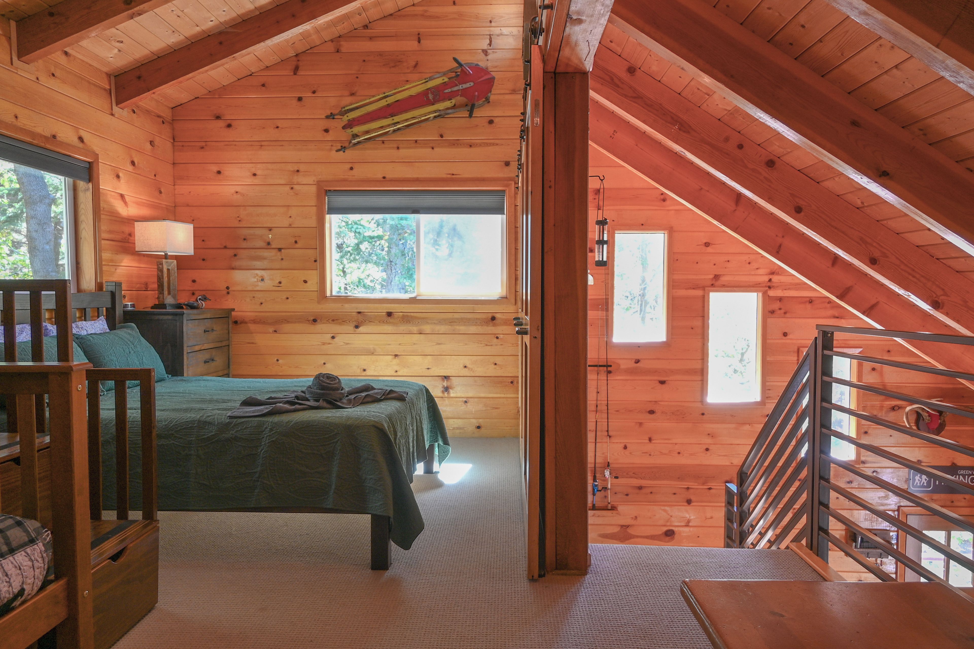 Ein Schlafzimmer einer Holzhütte mit einem Bett, einem Nachttisch, einer Lampe und einem Fenster.