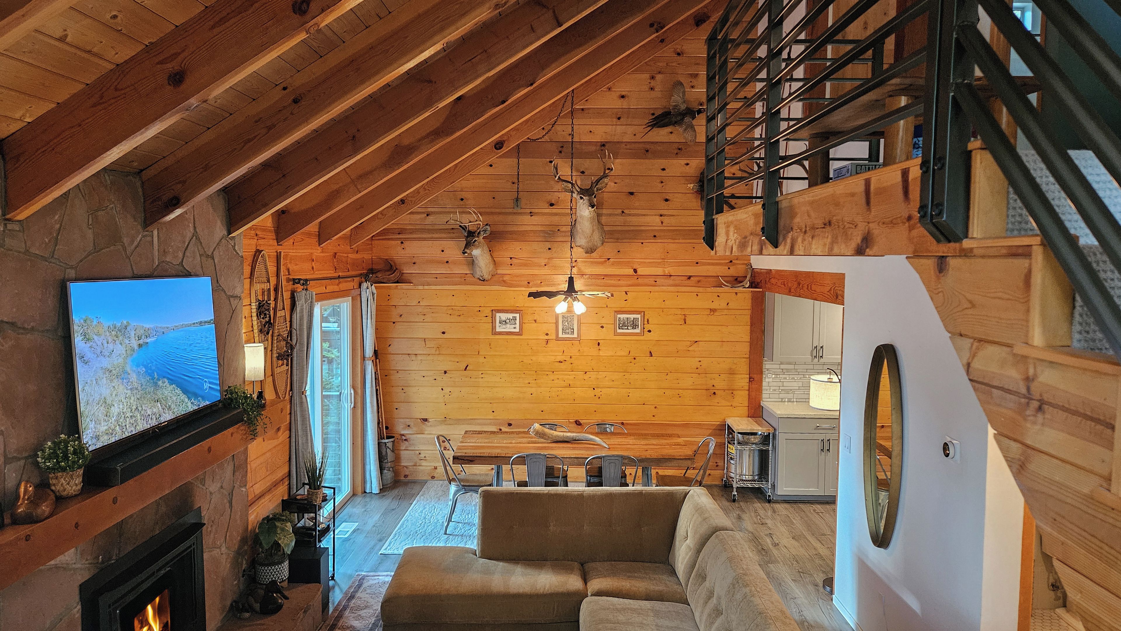 A cozy cabin interior with a fireplace, wooden walls, a sofa, and a kitchen area.