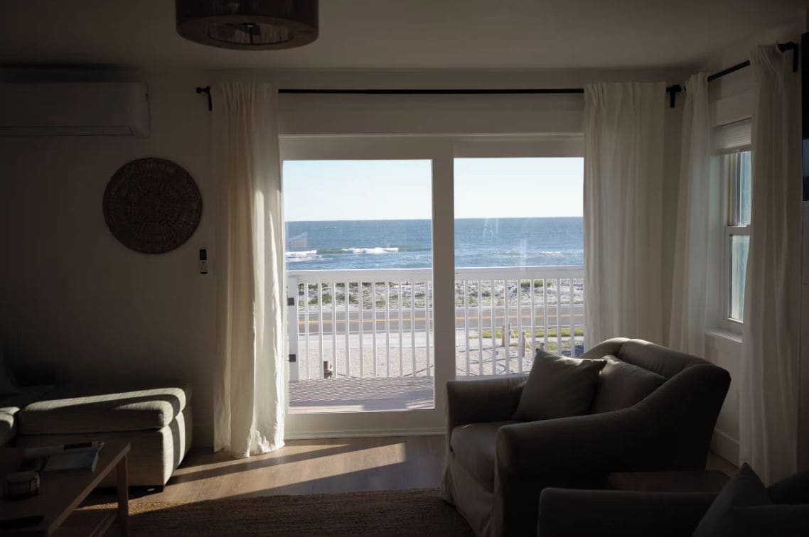 A living room with a sofa, a coffee table, and a view of the beach through a large window.