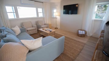 A living room with a sofa, armchairs, a coffee table, a TV, and a window.