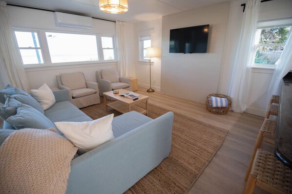 Una sala de estar con sofá, sillones, una mesa de centro, televisor y ventana con cortinas.