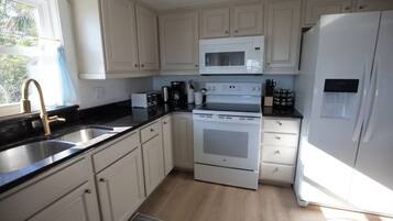 A kitchen with white cabinets, a stainless steel sink, a microwave, a stove, and a refrigerator.