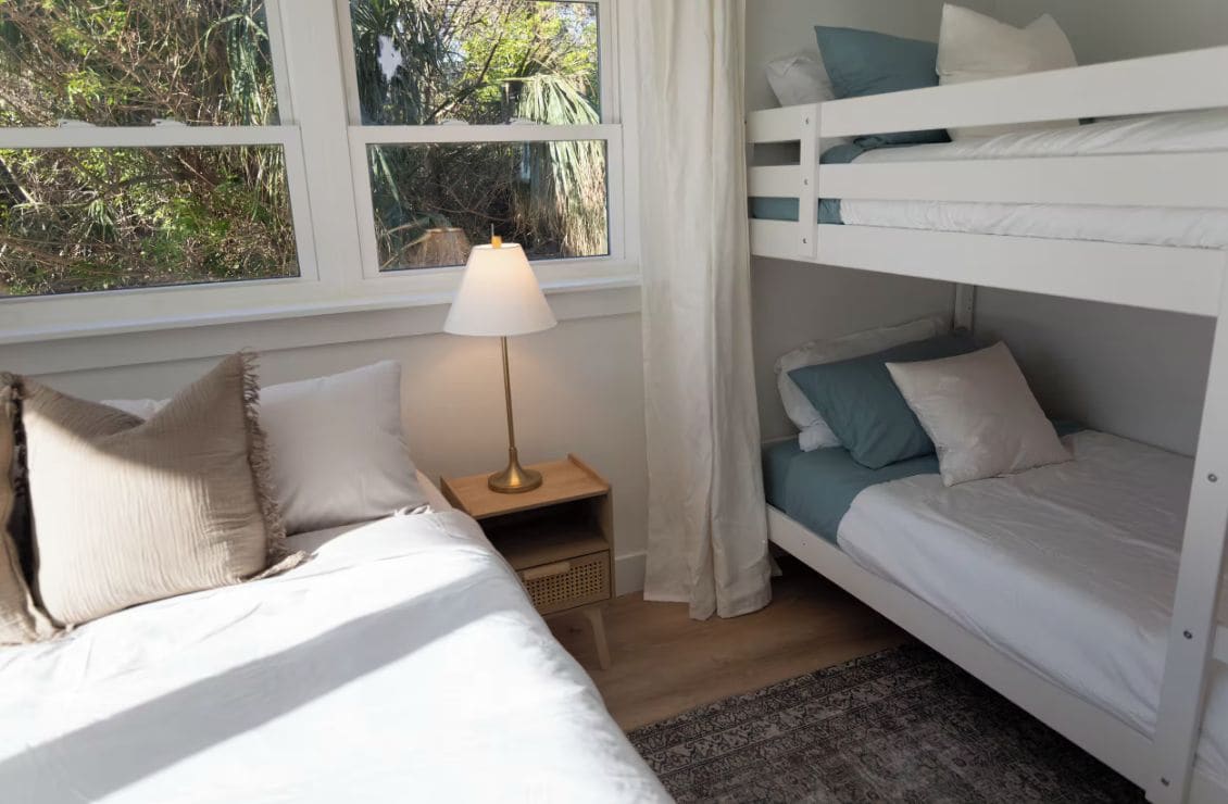 A room with bunk beds, a bedside table with a lamp, and a window with curtains.