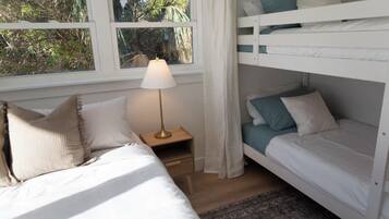 A room with bunk beds, a bedside table with a lamp, and a window with curtains.