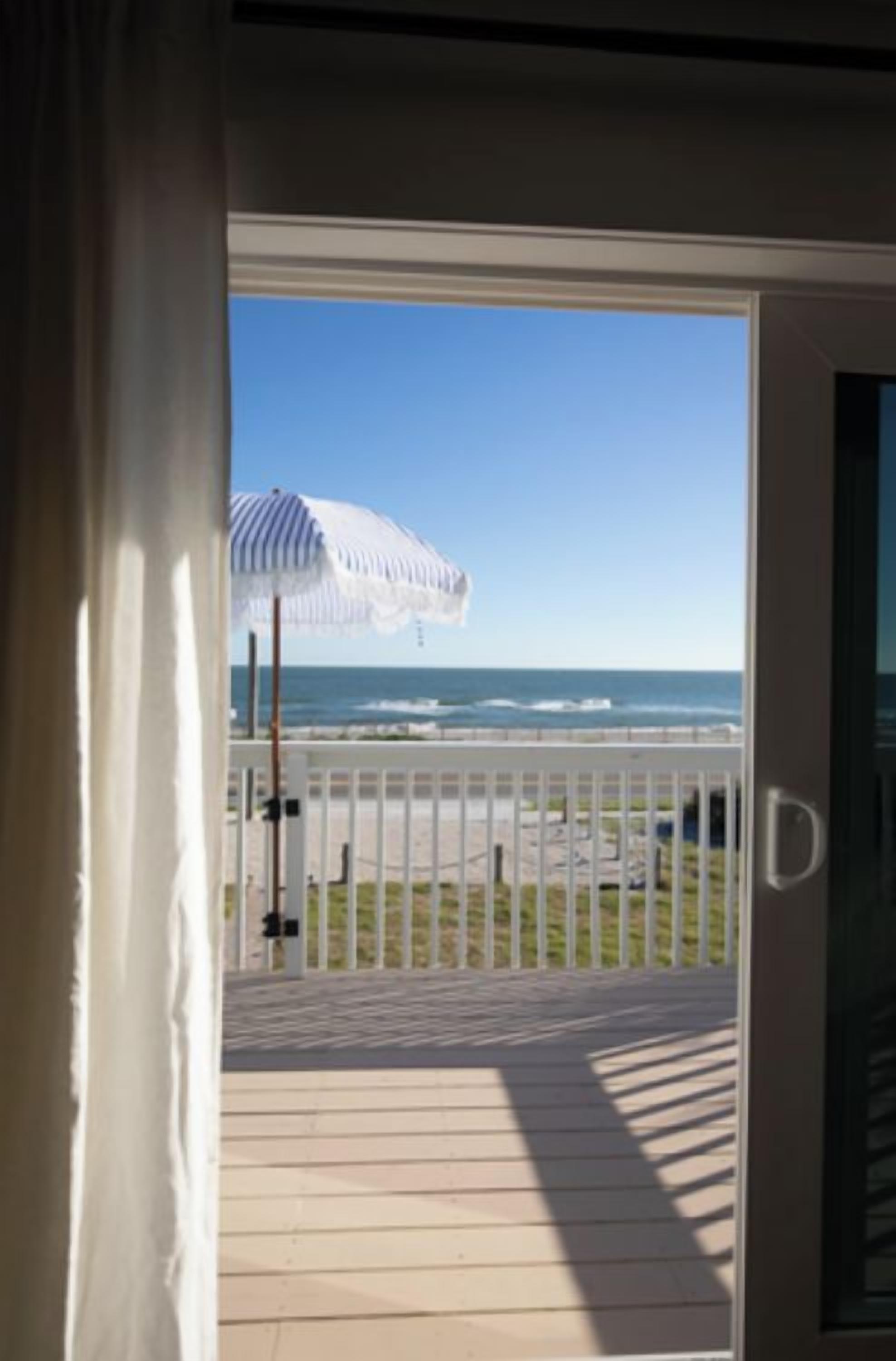 Vista desde una habitación a una playa con una sombrilla blanca y una terraza de madera.