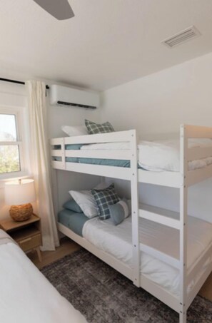 A bunk bed with white bedding, a bedside table with a lamp, and a window with curtains. - Ocean Front Flagler Beach Home (Flagler Beach)