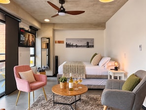 A modern hotel room with a bed, a seating area with a table, a television, and a cityscape painting. - Amazing Loft in Medellín—Central (Medellín)