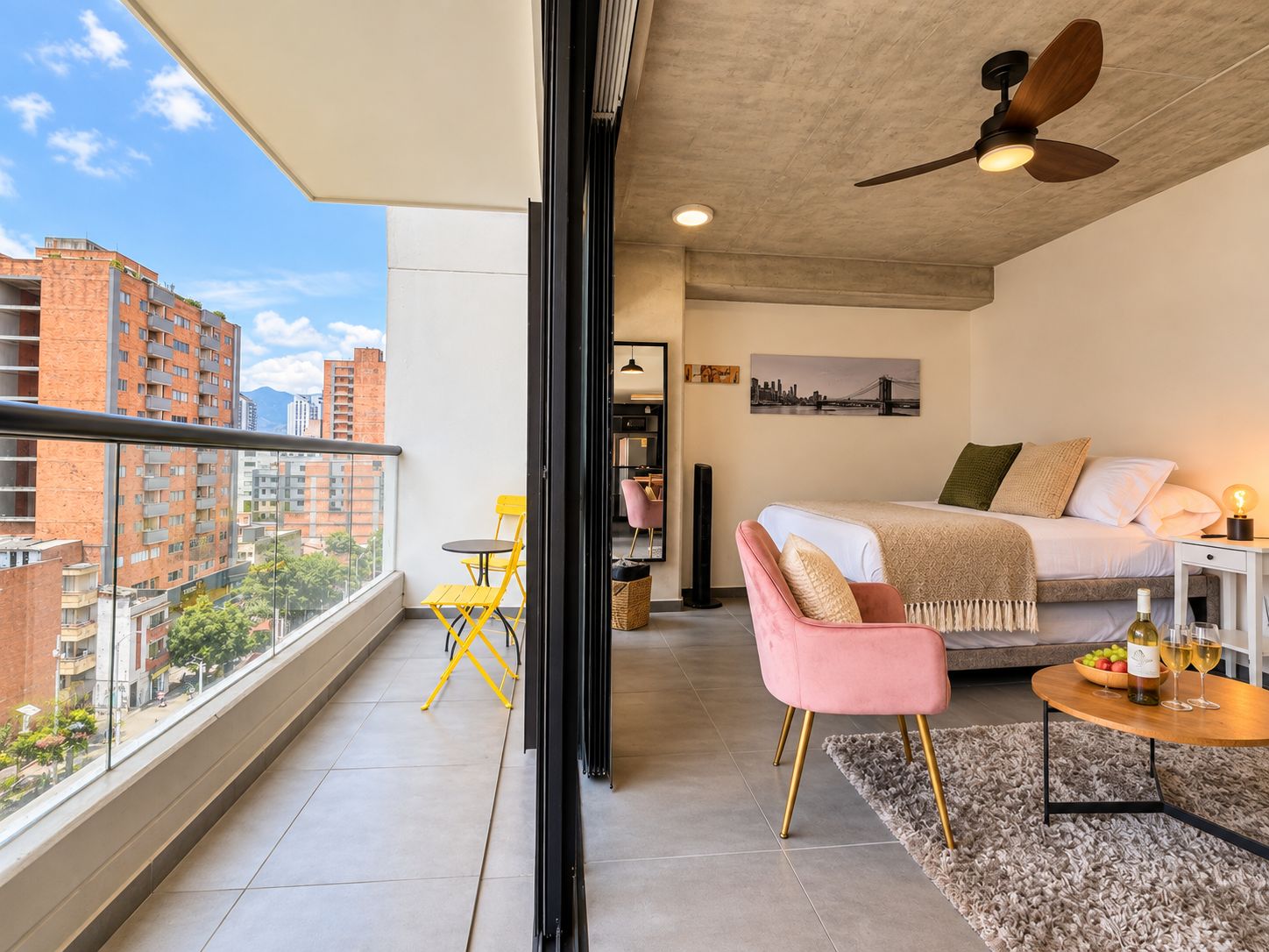 A modern apartment with a balcony, a bed, a dining area, and a city view.