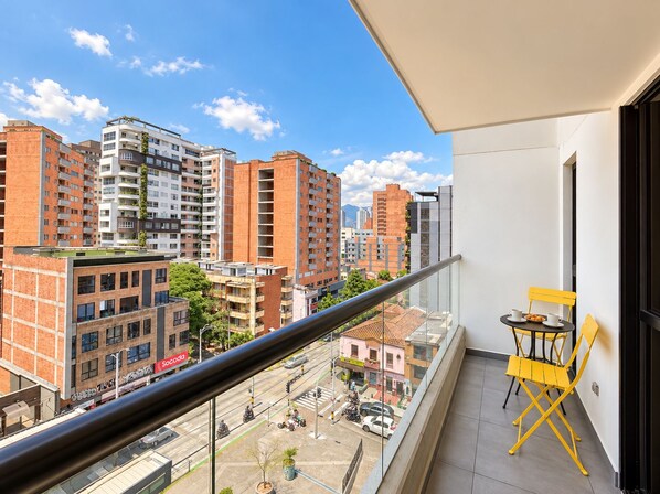 Uma varanda com vista para a paisagem urbana, mostrando edifícios altos e uma rua abaixo.