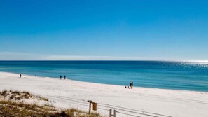 Une plage avec un ciel dégagé, un rivage sablonneux et quelques personnes qui se promènent.